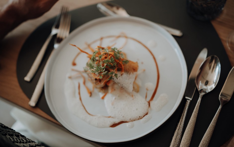 Ein kunstvoll angerichtetes Gericht auf einem wei&szlig;en Teller mit Besteck daneben